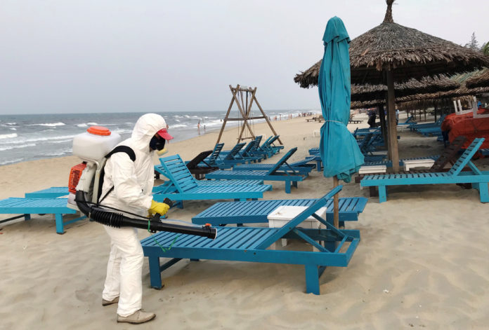 FILE PHOTO: A health worker sprays disinfectants to protect against the coronavirus on a beach in Hoi An