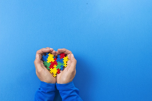 World autism awareness day concept. Child hands holding colorful puzzle heart on blue background DOCU_GRUPO