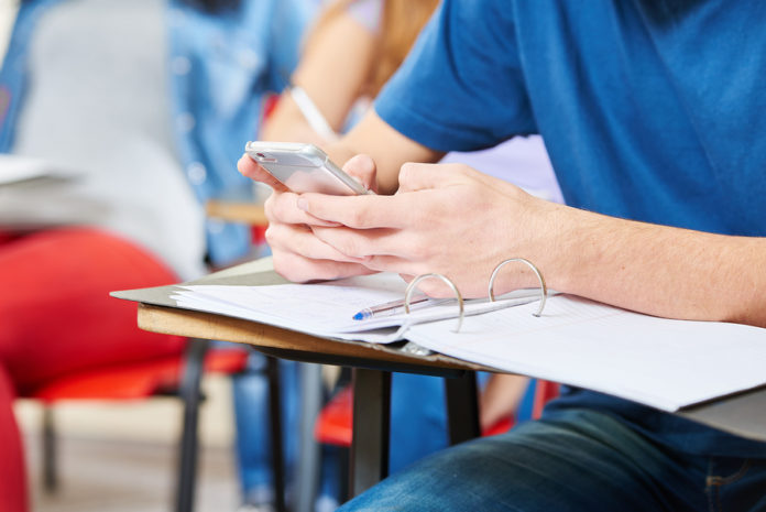 Student texting in class with his smartphone at school